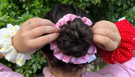 Persona ajustando un moño con un scrunchie floral rosa y otros scrunchies de tela en las muñecas.