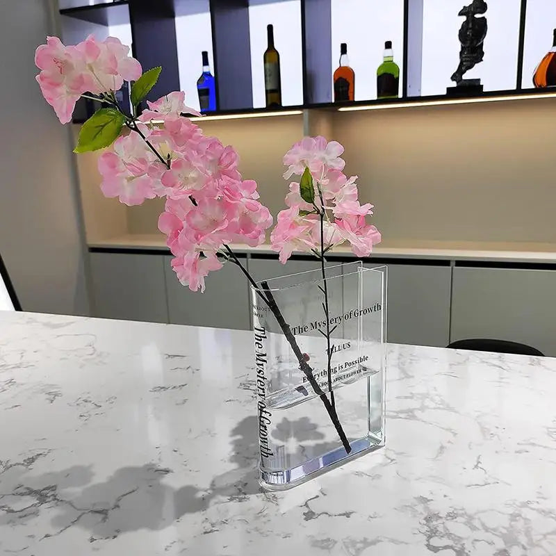 Clear acrylic vase with pink flowers on a marble surface — a modern home decor accent for minimalist interiors.