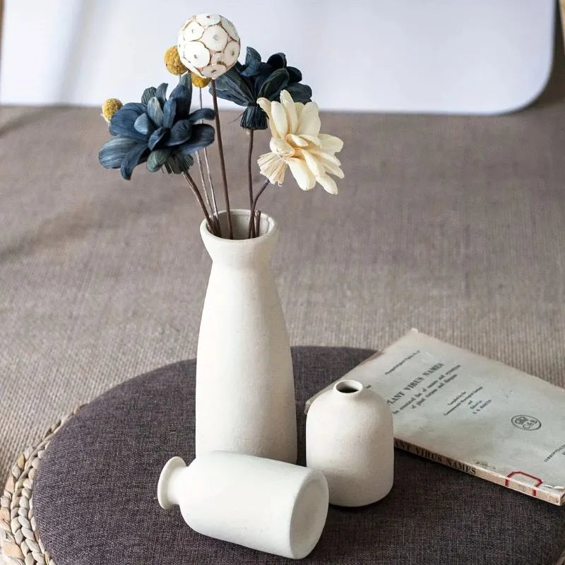 Two white vases with dried flowers on a textured surface